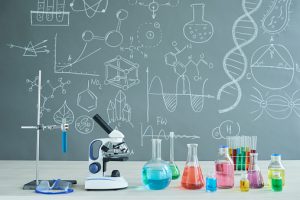 Interior of modern chemistry classroom: desk with microscope and laboratory glassware, blackboard with inscriptions, no people